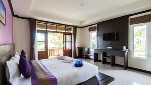 Habitación de hotel con cama, escritorio, televisor y ventana con vista a follaje.