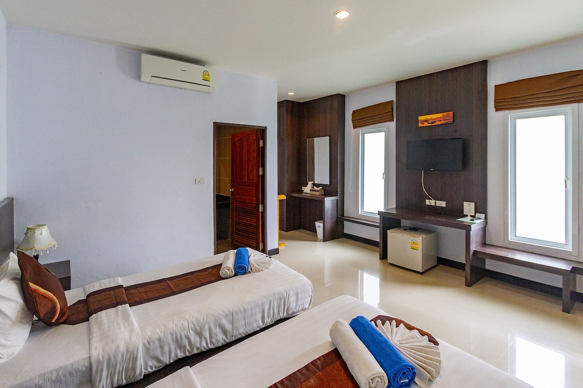 A hotel room with two beds, a desk, a TV, and an air conditioning unit.