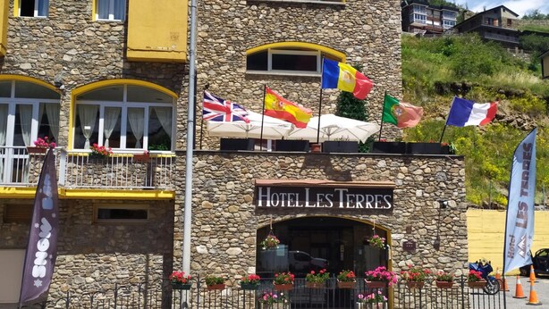 A hotel with a stone facade, multiple flags, and flower boxes. - Hotel Les Terres (Canillo)