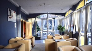 A hotel lobby with beige sofas and tables, large windows with curtains, and a view of the outdoors. - Hotel Les Terres (Canillo)