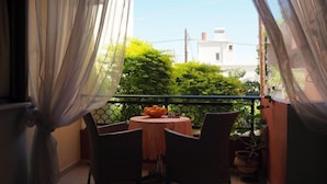 Un balcón con mesa y sillas, un frutero y vistas a zonas verdes y edificios.