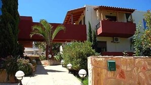 Un edificio de techo rojo y paredes blancas, una pared de piedra con un letrero verde, y un camino con faroles.