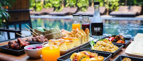 A buffet with various dishes, drinks, and a poolside setting.
