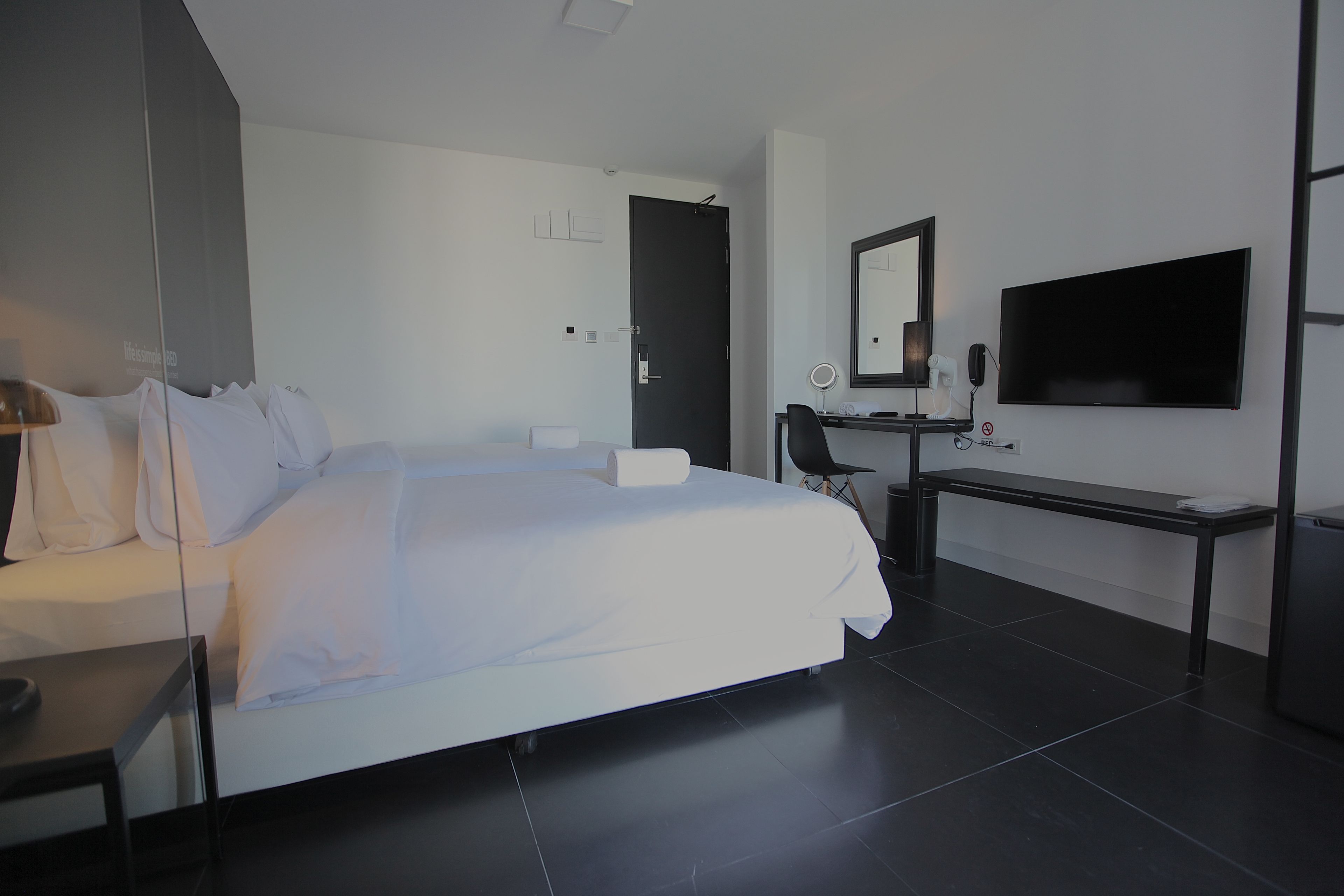 A modern hotel room with a large bed, a desk, a chair, a TV, and a mirror.