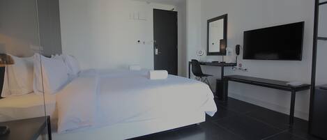 A modern hotel room with a large bed, a desk, a chair, a TV, and a mirror.