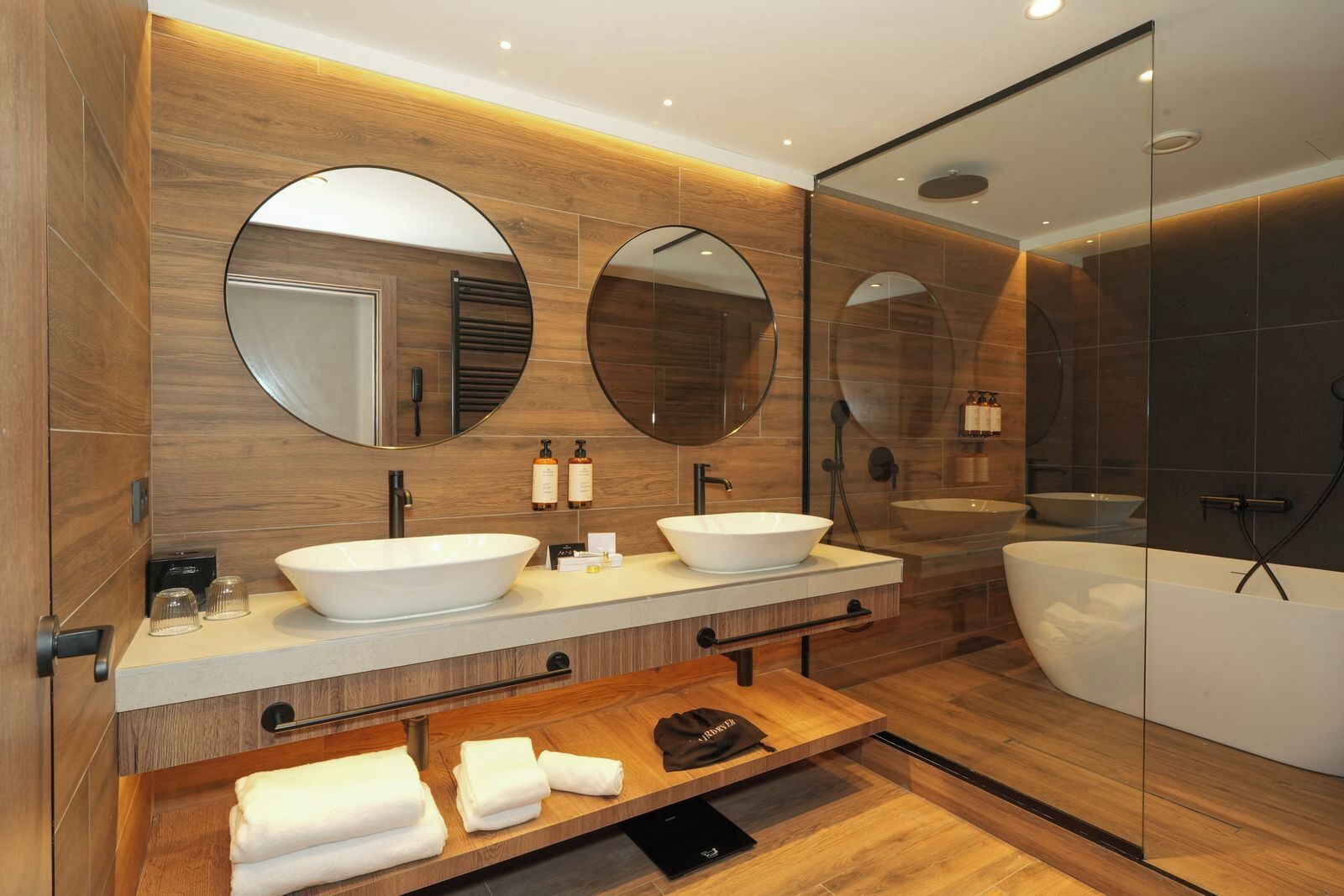 Een moderne badkamer met twee ruime wastafels, een badkuip en een douchecabine met glazen wanden.