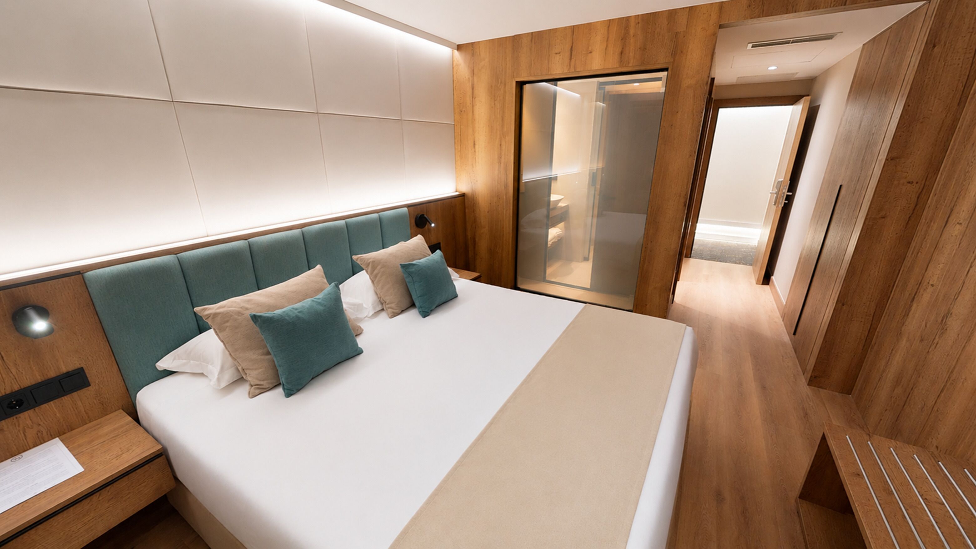 Una habitación de hotel moderna con una cama grande, paneles de madera, una puerta corrediza de cristal y una mesita de noche con una lámpara.
