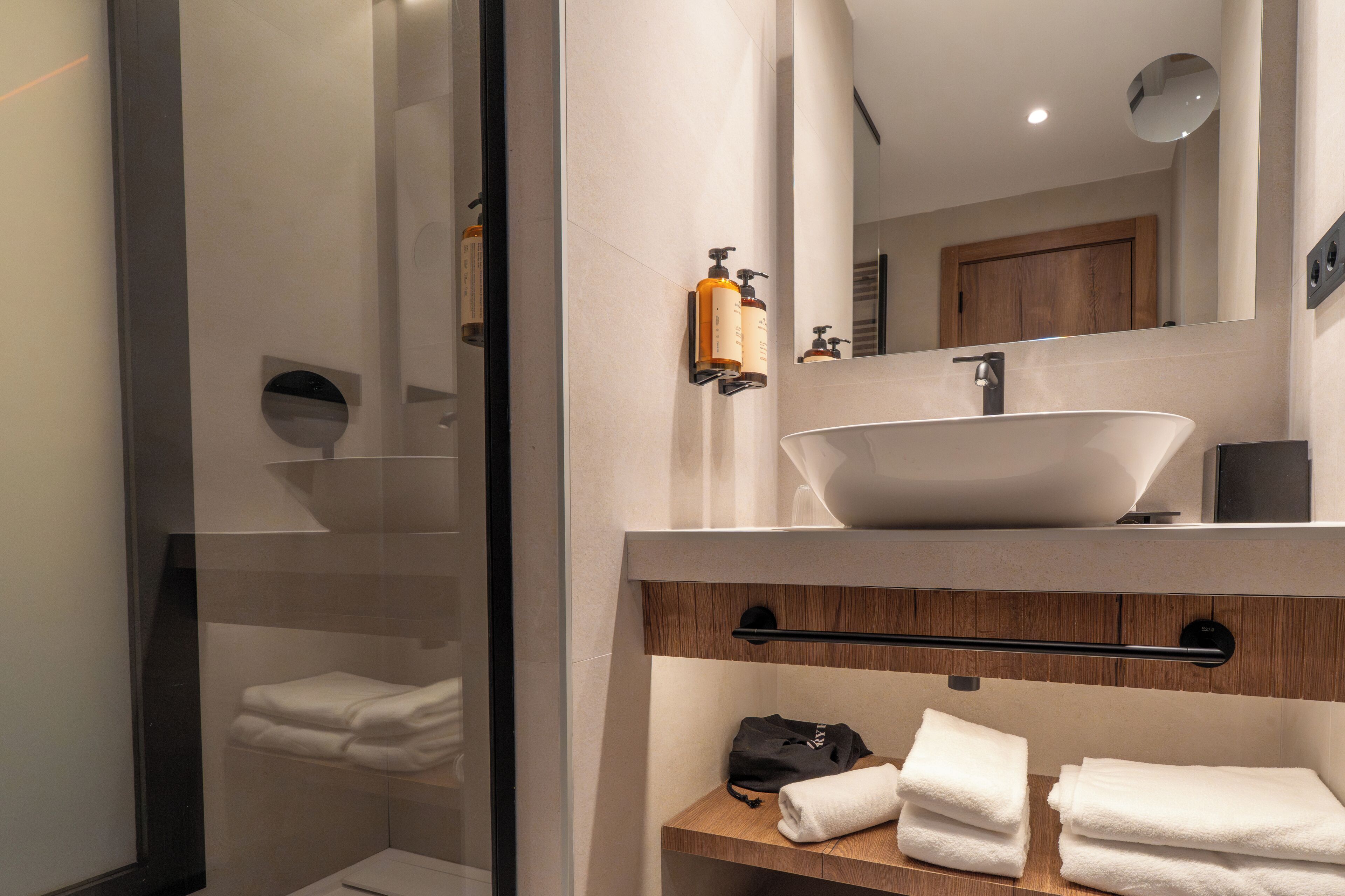 Un baño moderno con un espejo grande, un lavabo sobre encimera y toallas dobladas en un estante de madera.