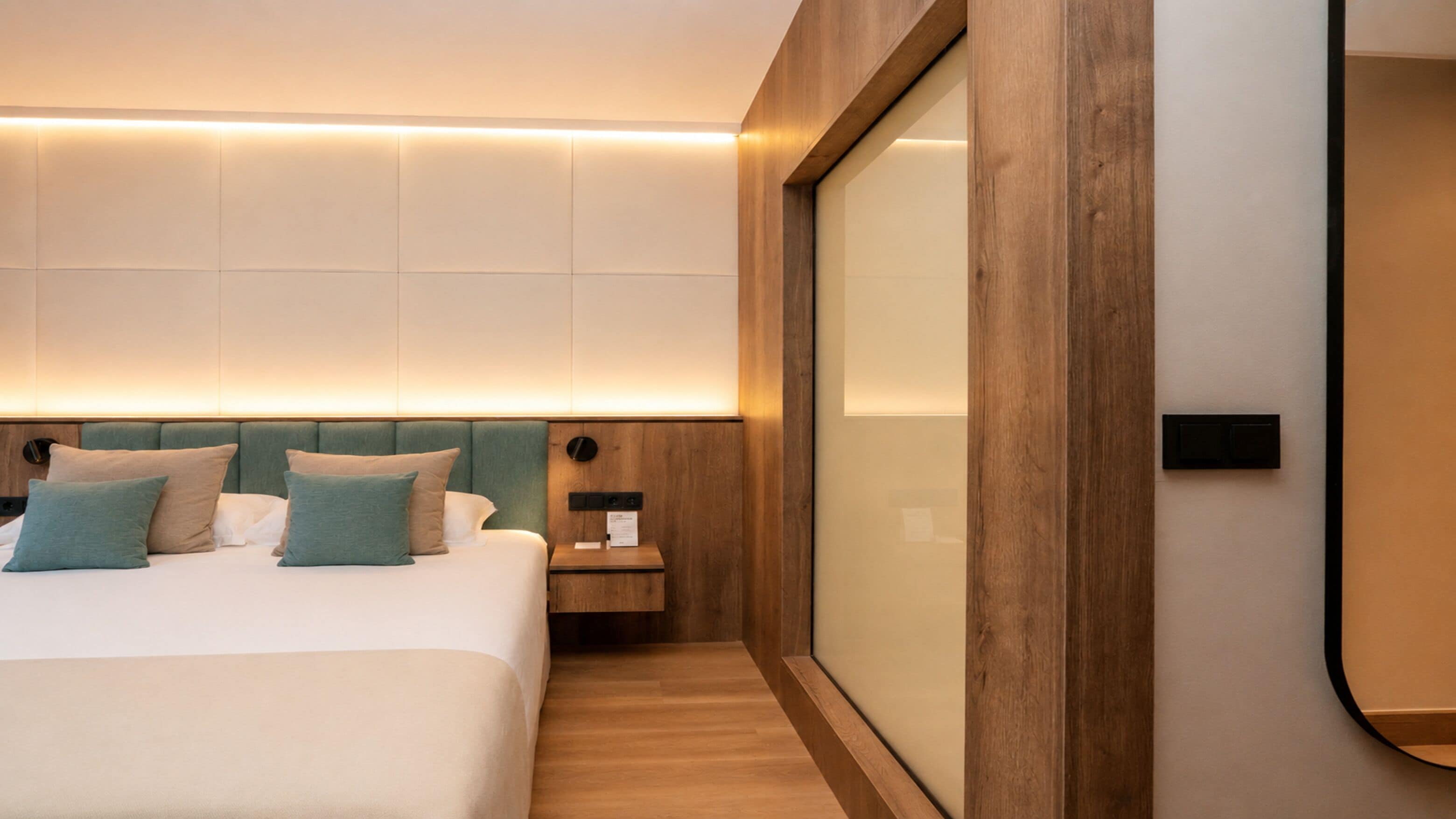 Een moderne hotelkamer met een groot bed, nachtkastje, houten hoofdbord en grote spiegel.