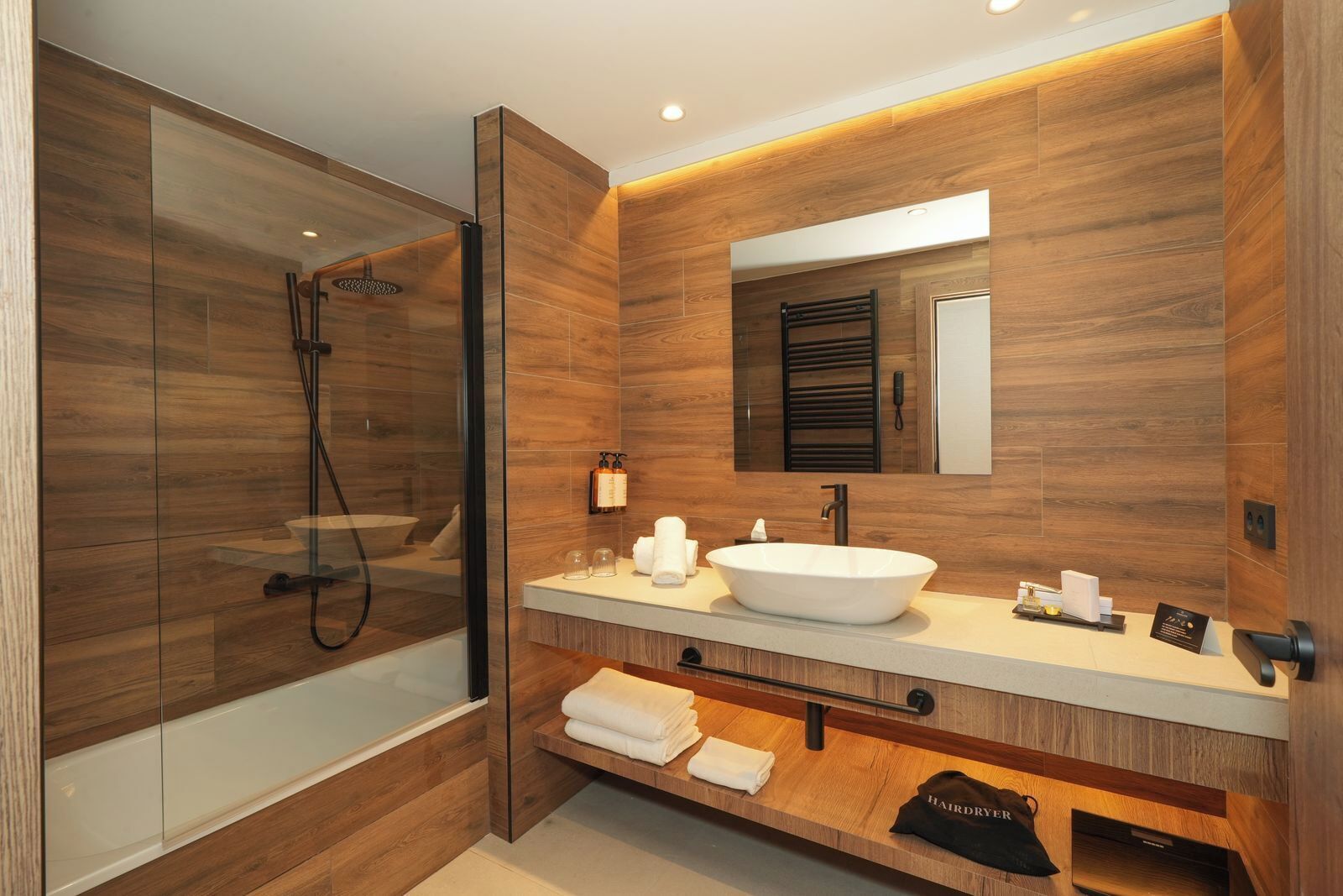 Un baño moderno con ducha de vidrio, lavamanos blanco y paneles de madera.