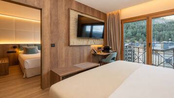 A hotel room with a bed, a desk, a TV, and a balcony with a view of trees.