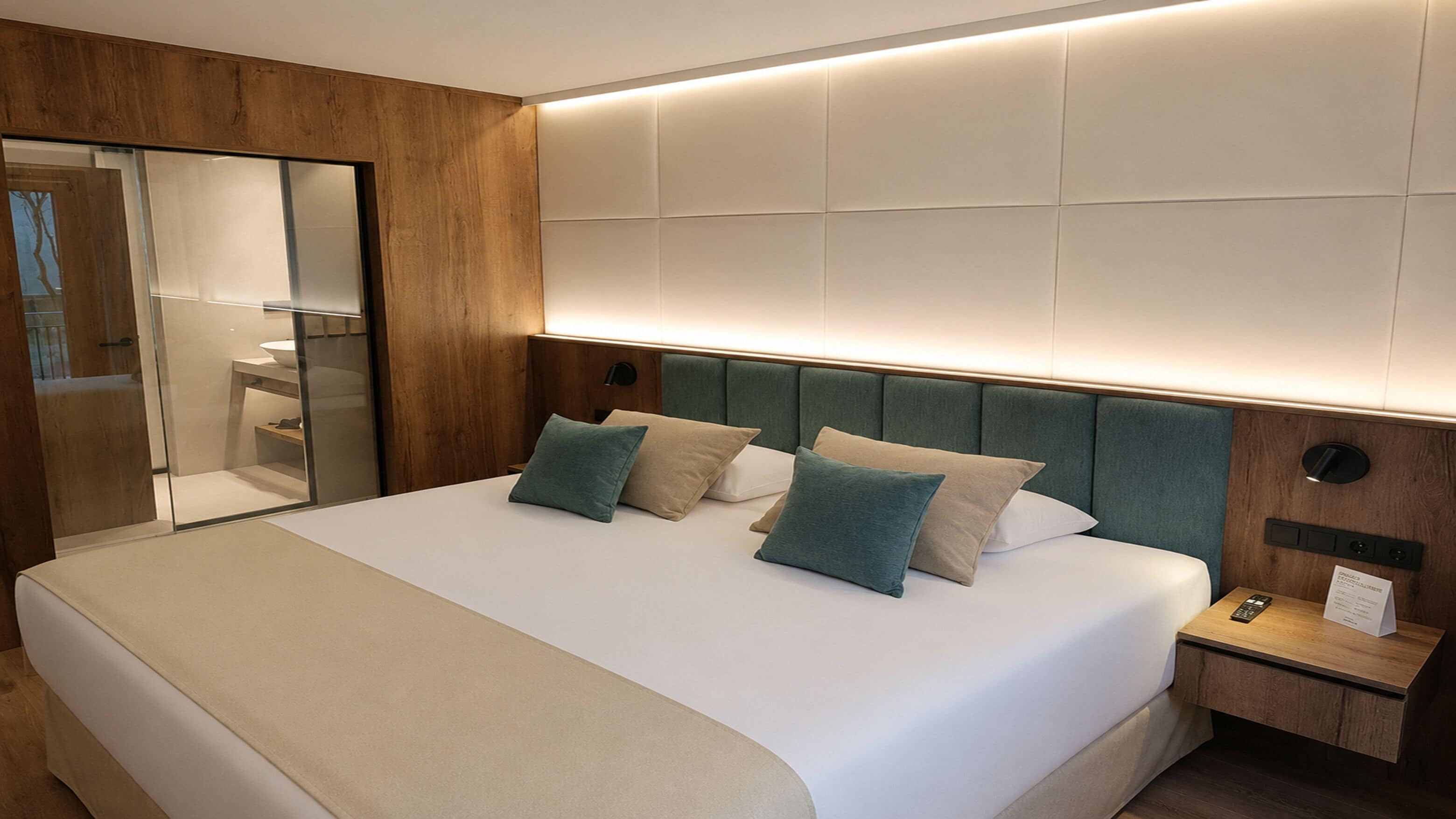Una habitación de hotel moderna con una cama grande, un armario de madera, una mesita de noche y un espejo.