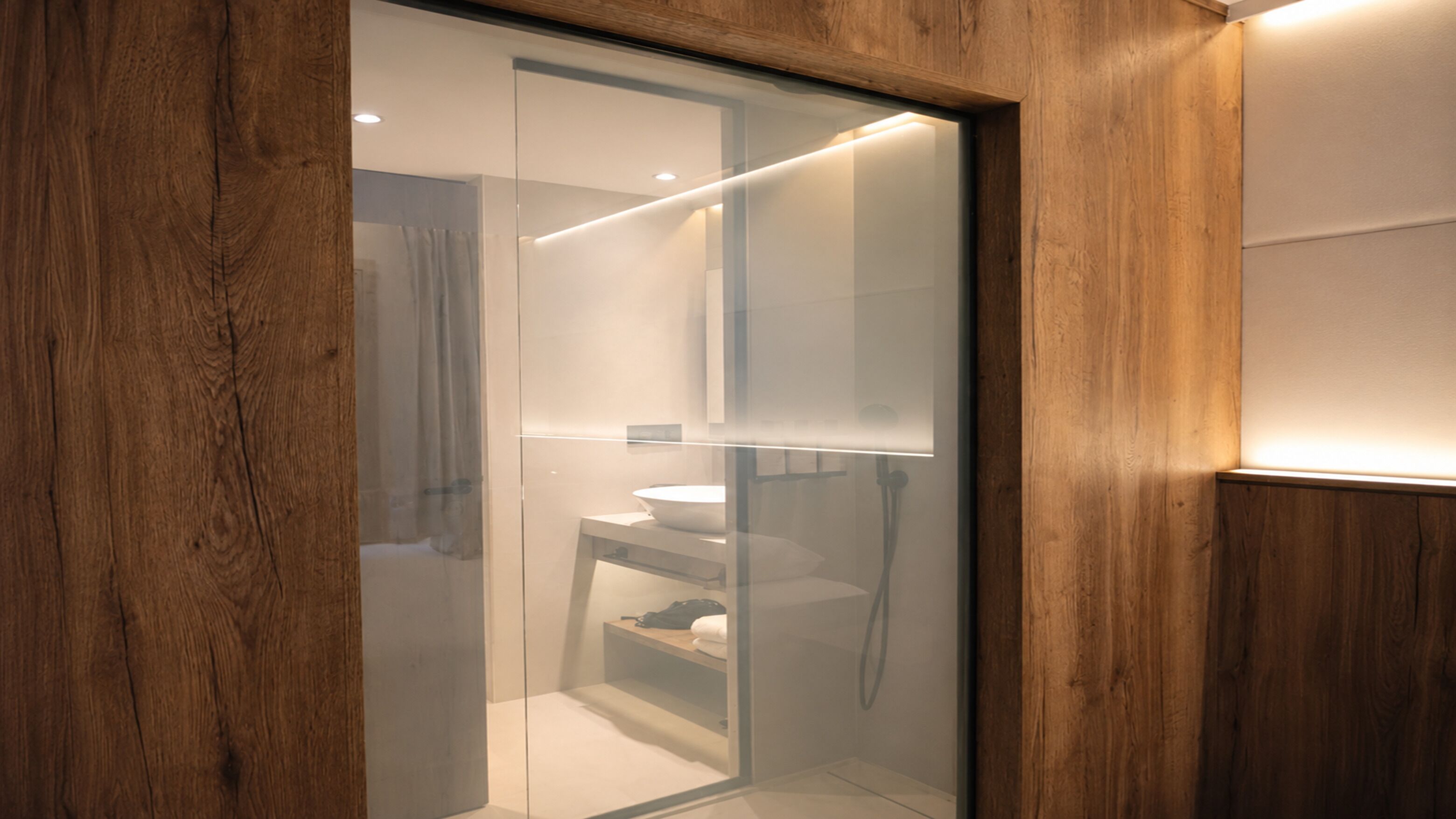 Een moderne badkamer met een douchecabine van glas, een witte wastafel en houten wandpanelen.