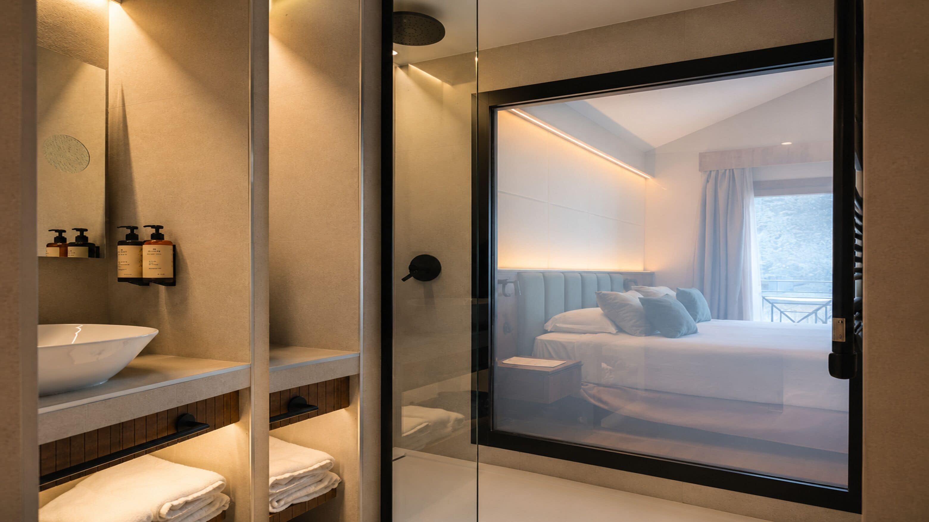 Un baño moderno con cabina de ducha de vidrio, un espejo grande y un lavamanos con artículos de aseo.