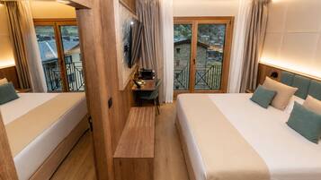 Et hotelværelse med to senge, et skrivebord, et fjernsyn og en balkon med udsigt til bygninger.