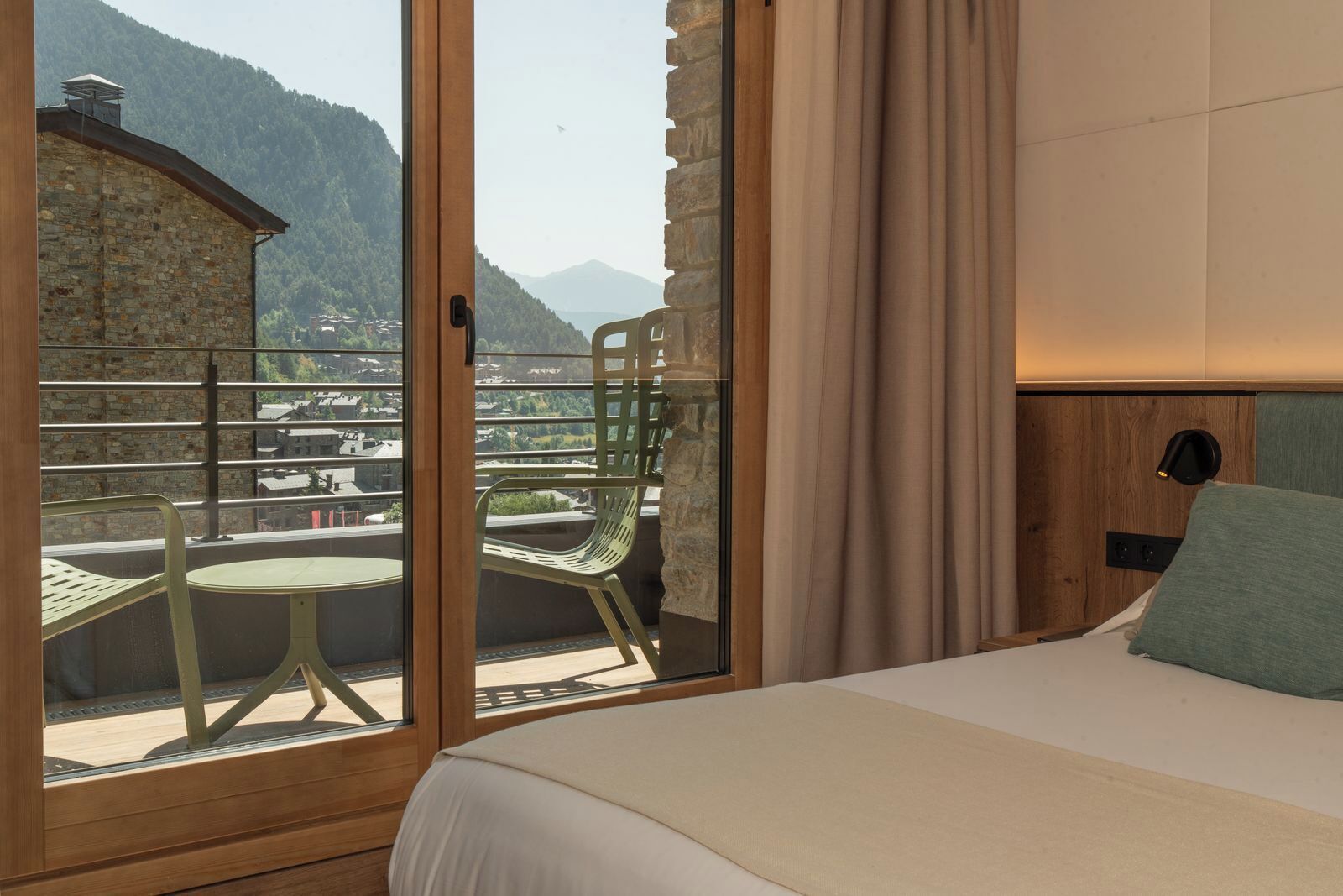 Habitación de hotel con una cama, ventana con vista a una montaña, una silla y una mesa.