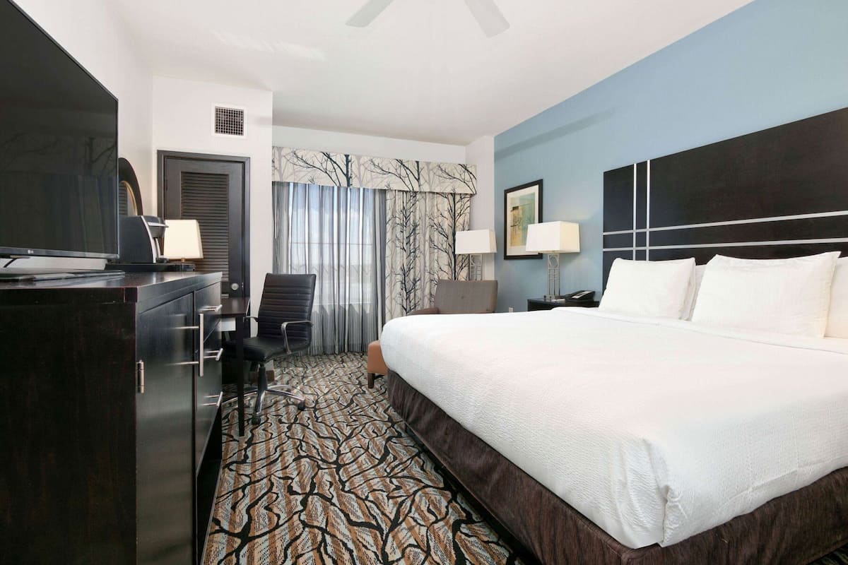 A hotel room with a bed, desk, chair, and a television.