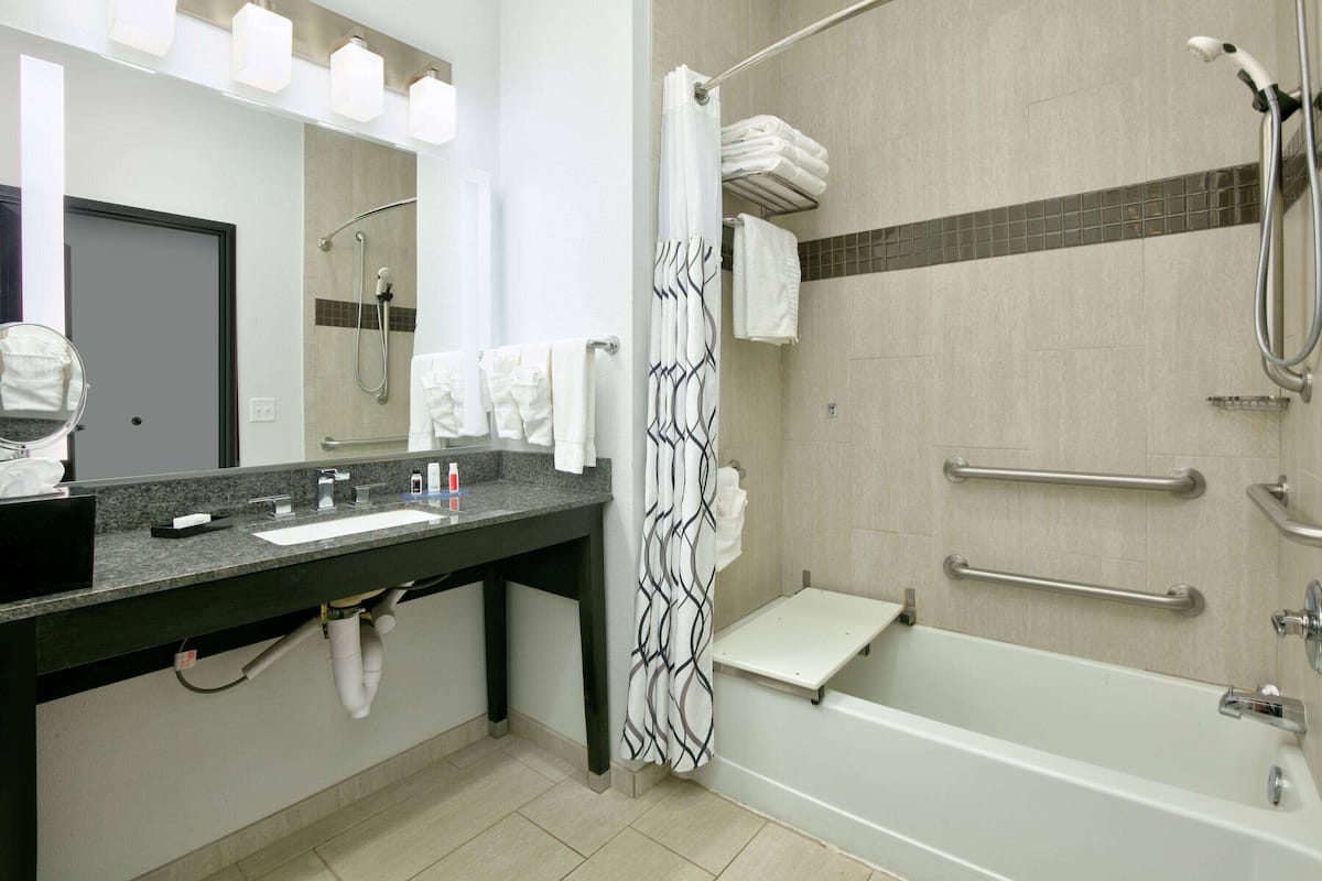 A modern bathroom with a sink, mirror, towel rack, shower, and grab bars.