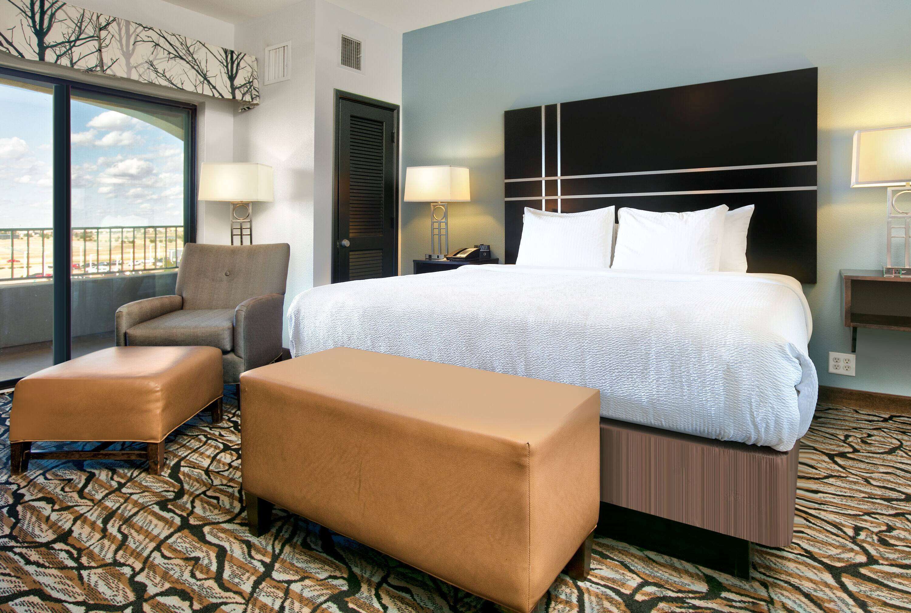 A hotel room with a large bed, two armchairs, a small table, and a view of the outdoors.