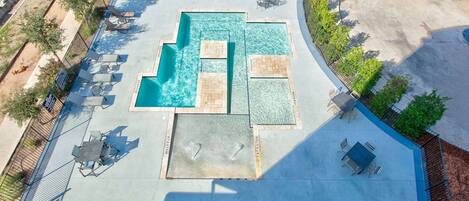 An aerial view of a swimming pool area with multiple lounge chairs and a table, surrounded by a fence and greenery.