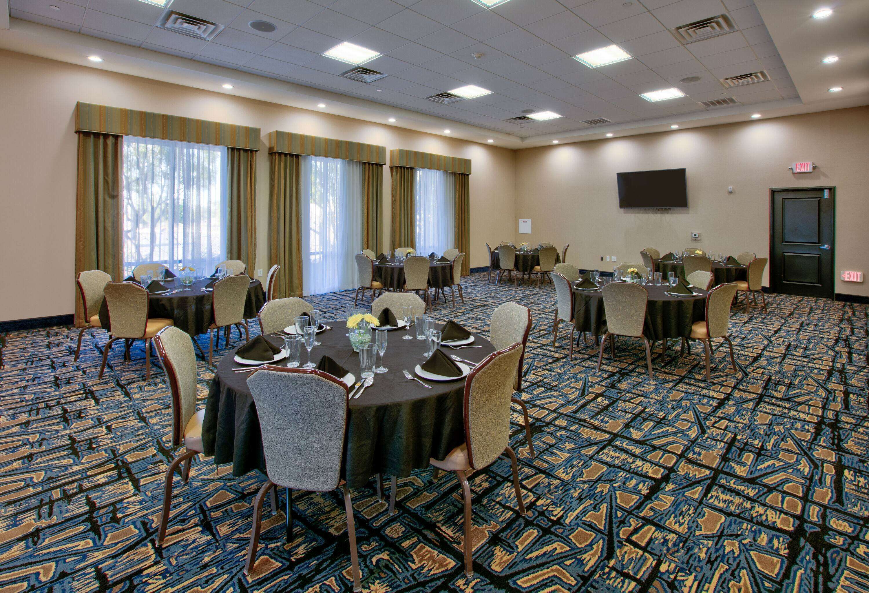 A conference room with multiple tables, chairs, and a large screen on the wall.