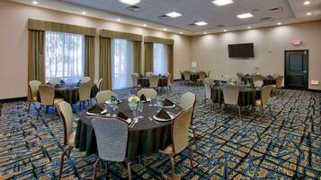 A conference room with multiple tables, chairs, and a large screen on the wall.
