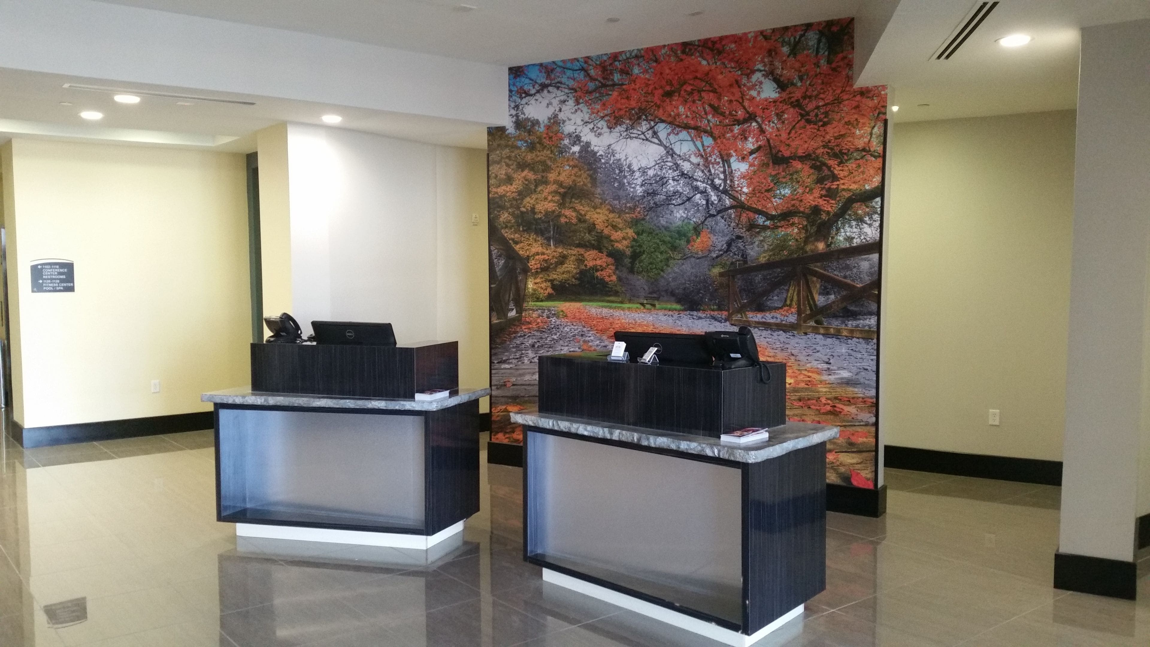 A reception area with two dark reception desks, a large autumn-themed mural on the wall, and a clean, tiled floor.