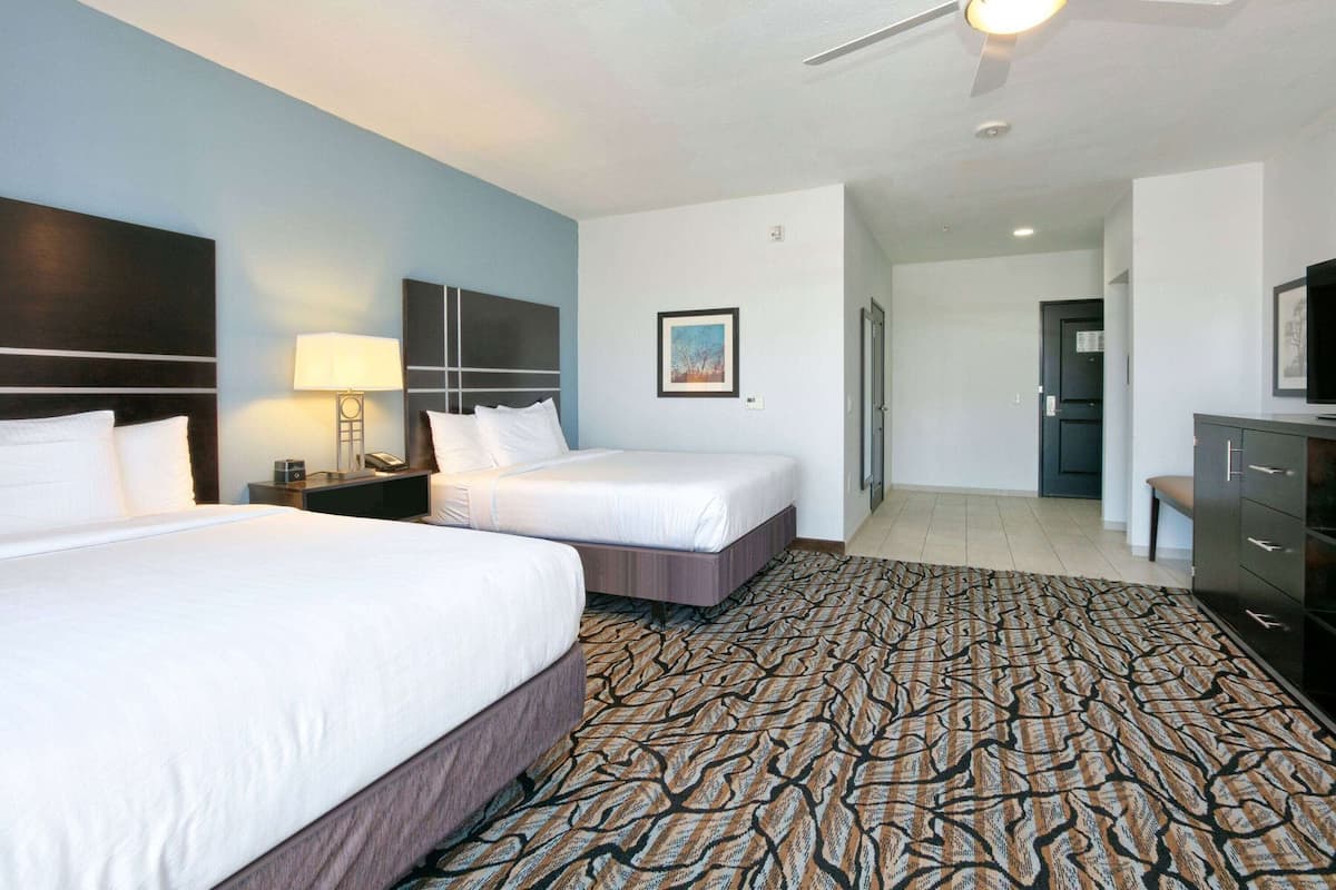 A hotel room with two beds, a desk, a chair, a television, and a patterned carpet.