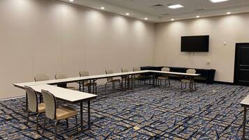 A conference room with a long table, chairs, a projector screen, and patterned carpet.