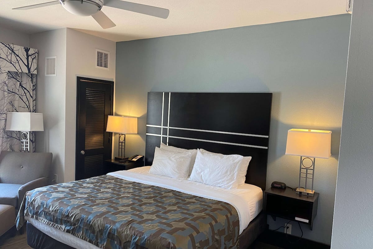 A hotel room with a bed, two bedside lamps, a chair, a desk with a lamp, and a ceiling fan.