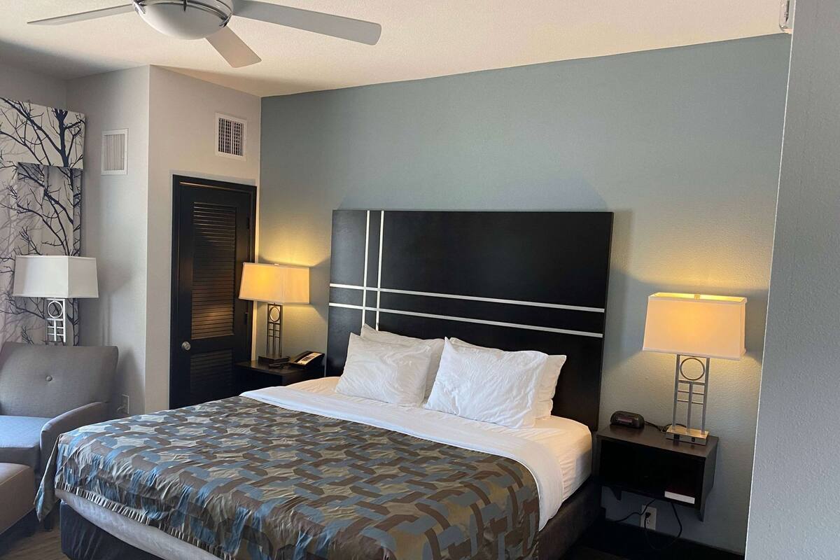 A hotel room with a bed, two bedside lamps, a chair, a desk, and a ceiling fan.