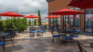 Un espace extérieur aménagé en terrasse, avec des tables et des chaises, des parasols rouges et un sol recouvert de dalles de pierre.