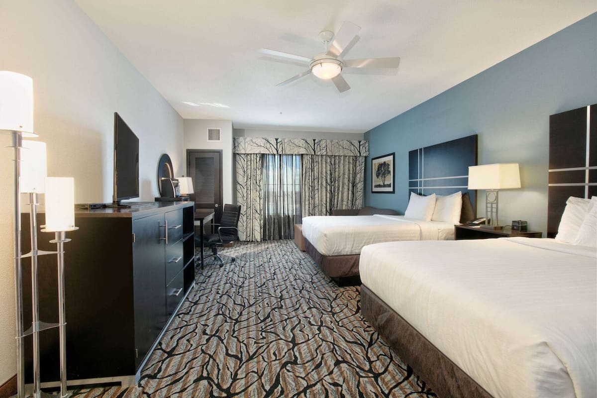 A hotel room with two beds, a desk with a chair, a wardrobe, and a patterned carpet.