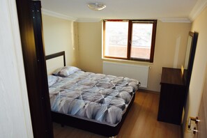 Un dormitorio con cama, radiador, ventana con persianas y puerta.