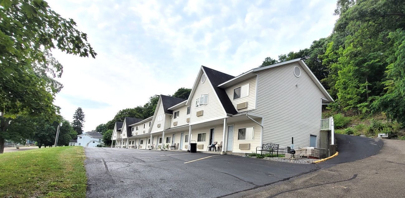 A row of motel-style buildings with a parking lot in front.