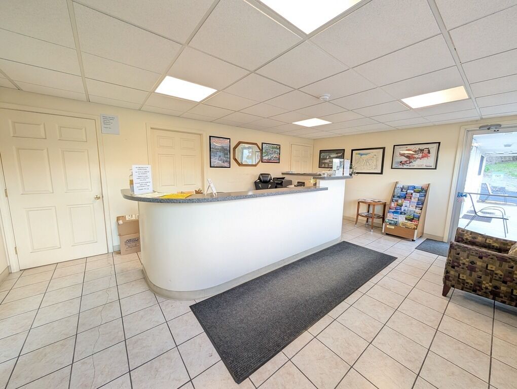 A reception area with a counter, a desk, and a chair. There are framed pictures on the wall, a door, and a window.