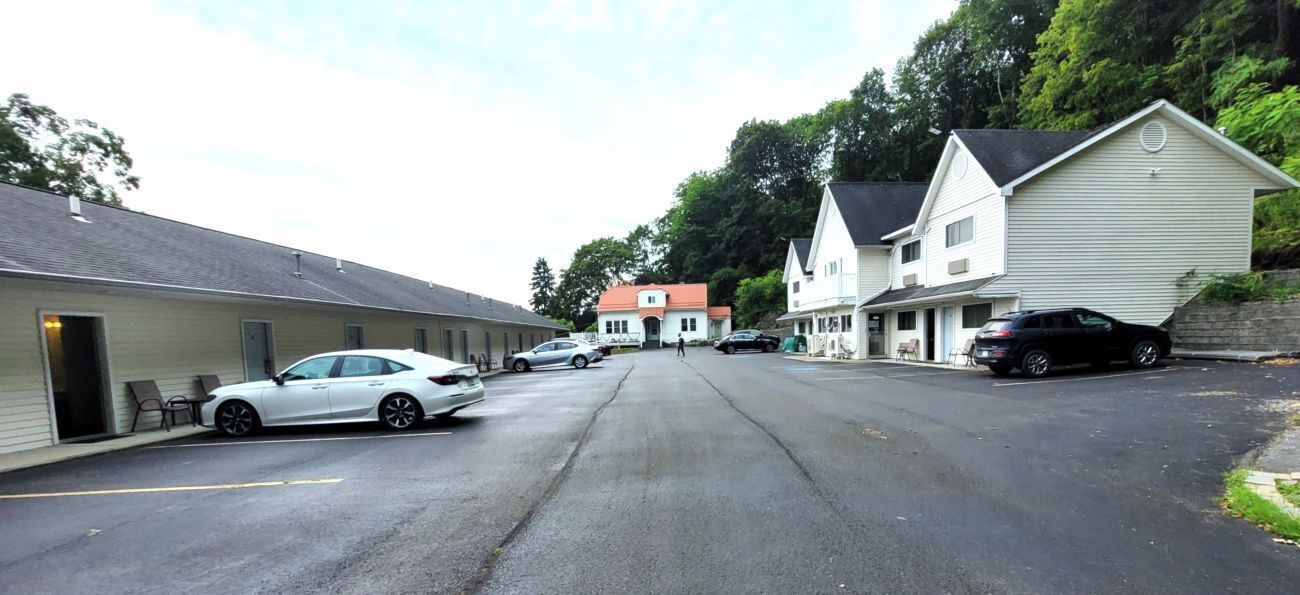 Une vue de rue avec une rangée de bâtiments, dont un motel devant lequel est garée une voiture.