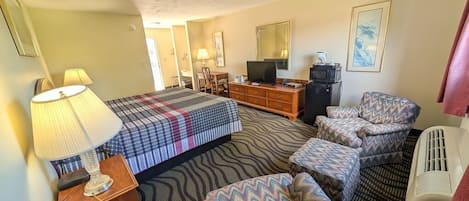 A hotel room with a bed, a desk, a television, a microwave, and a seating area with ottomans.