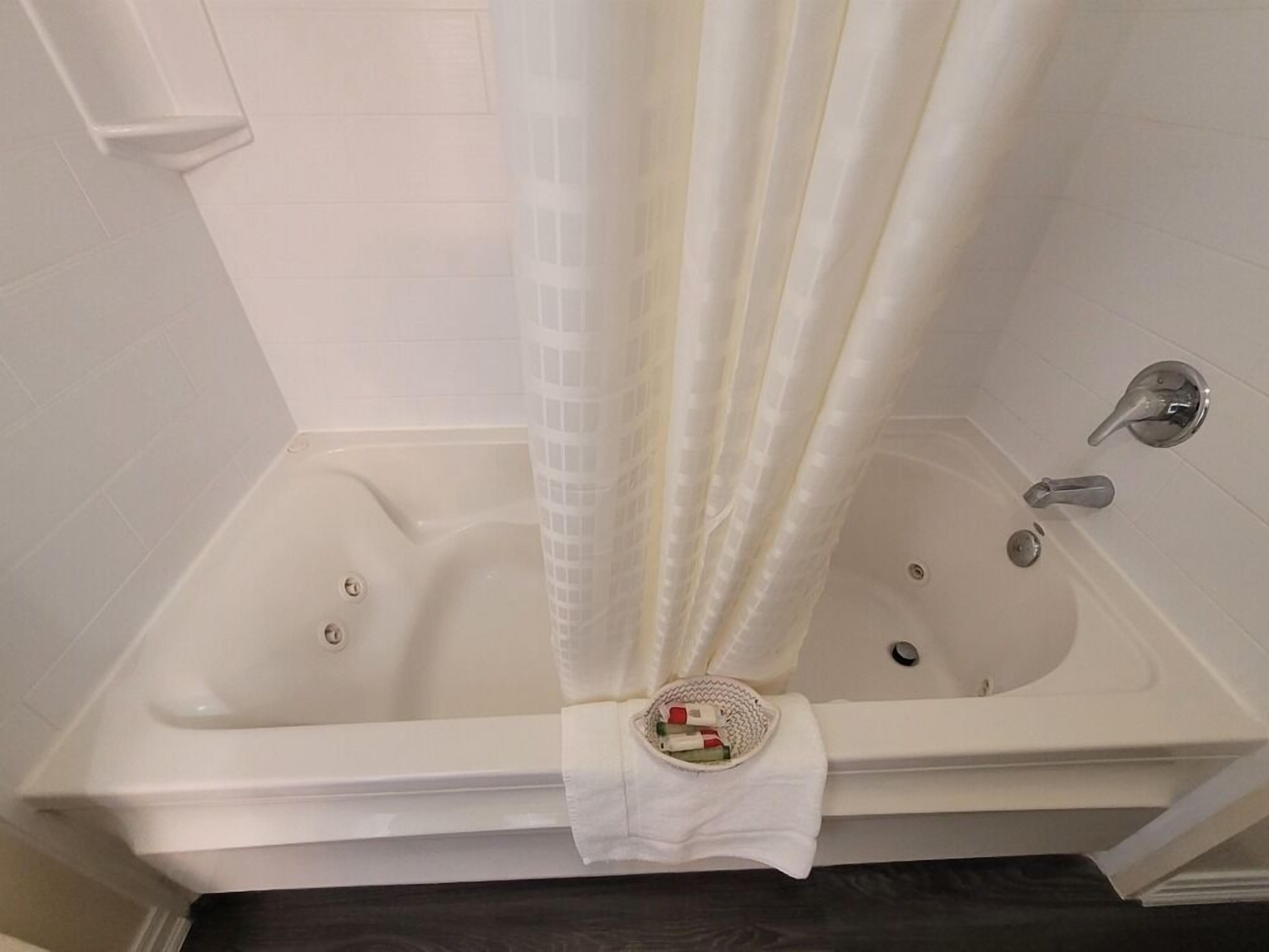 A white bathtub with a shower curtain, a small basket with toiletries, and a towel on the floor.