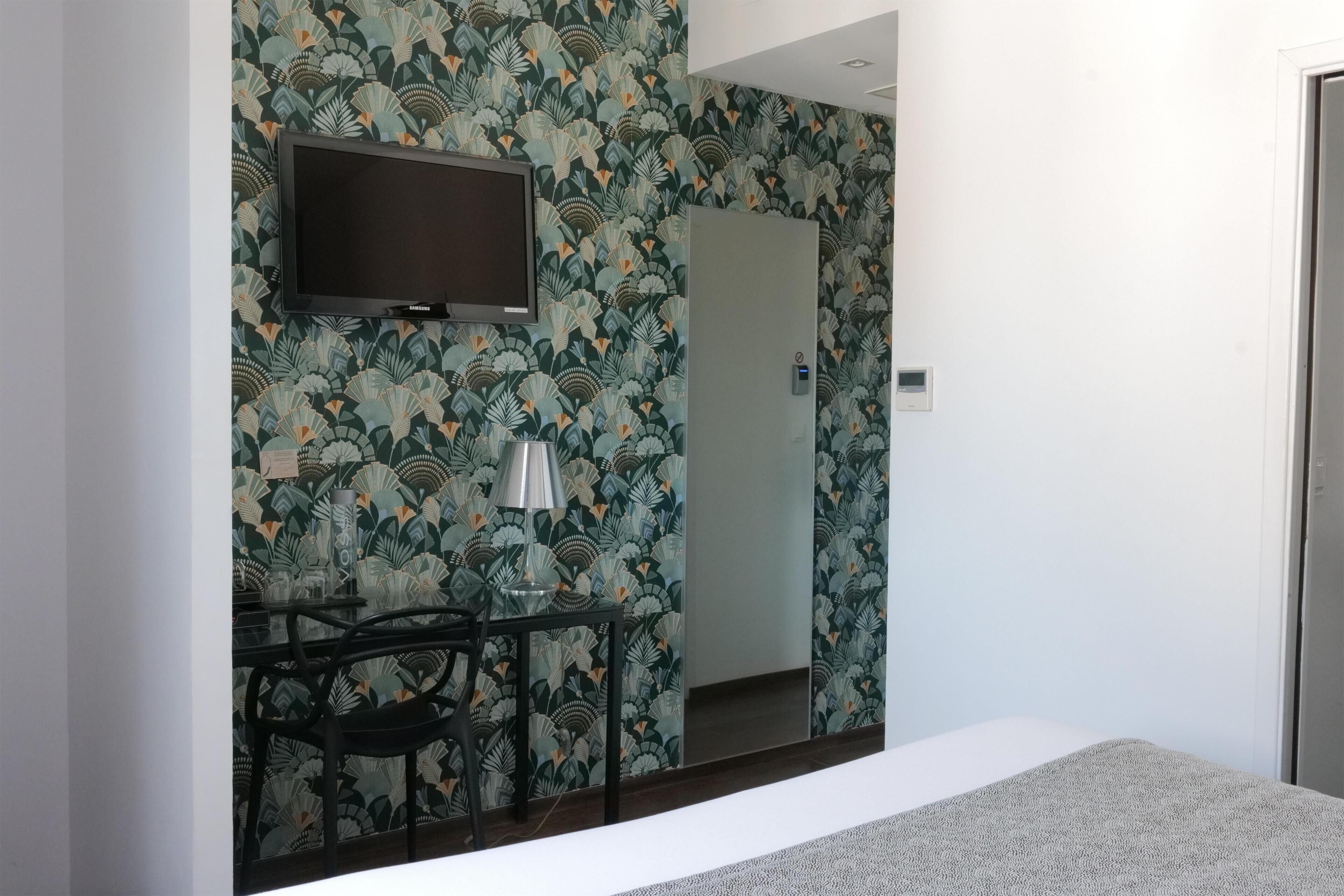 A hotel room with a bed, a desk with a chair, a television mounted on the wall, and a door with a mirror.