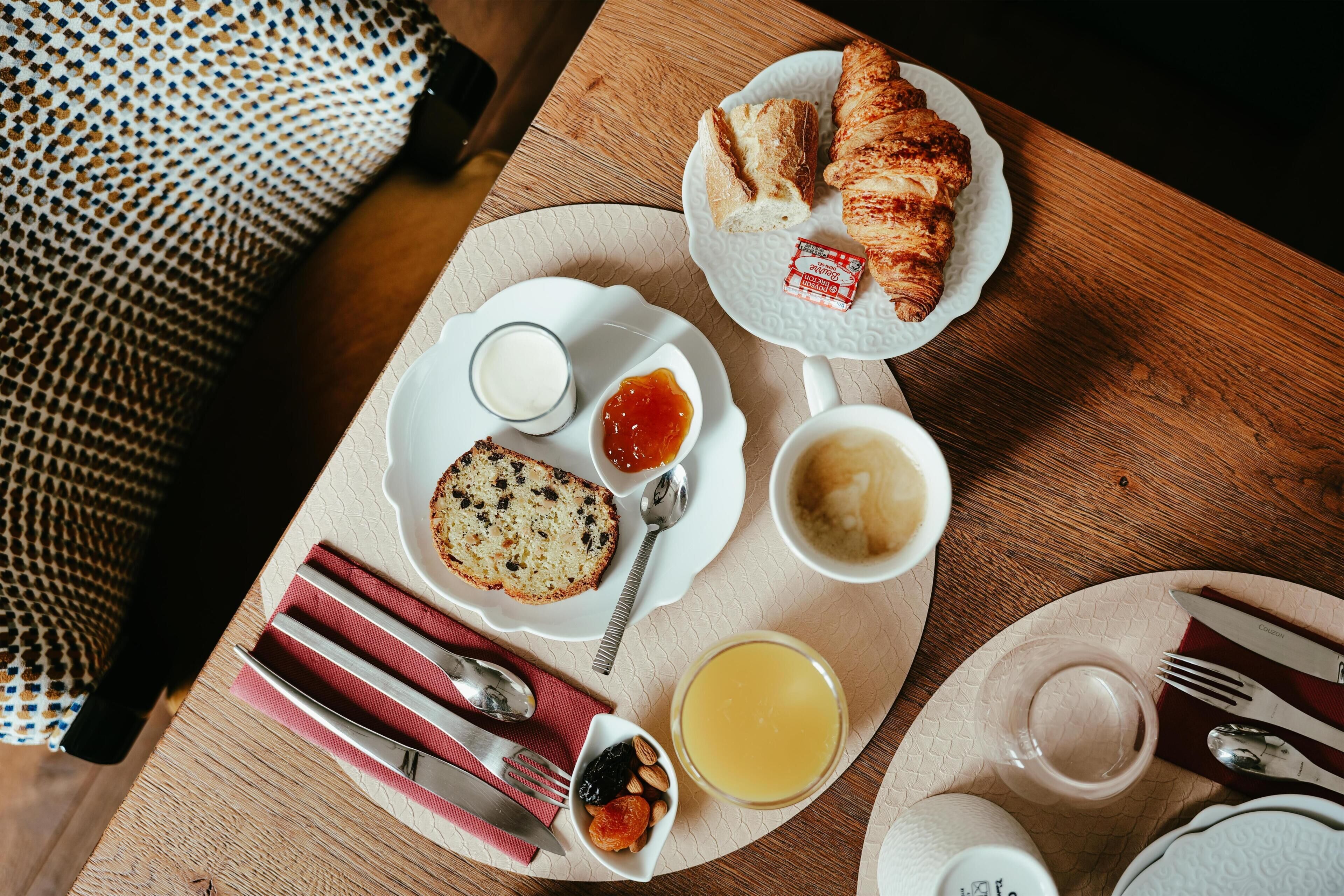 A breakfast setting with croissants, jam, butter, and a loaf of bread on a table.