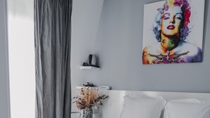 A modern bedroom with a large bed, a grey curtain, a white bedside table with a vase, and a colorful artwork on the wall. - Le Manoir Hotel, BW Signature Collection (La Rochelle)