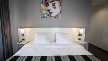 A hotel room with a large bed, two bedside tables, a wall-mounted artwork, and a window with curtains.