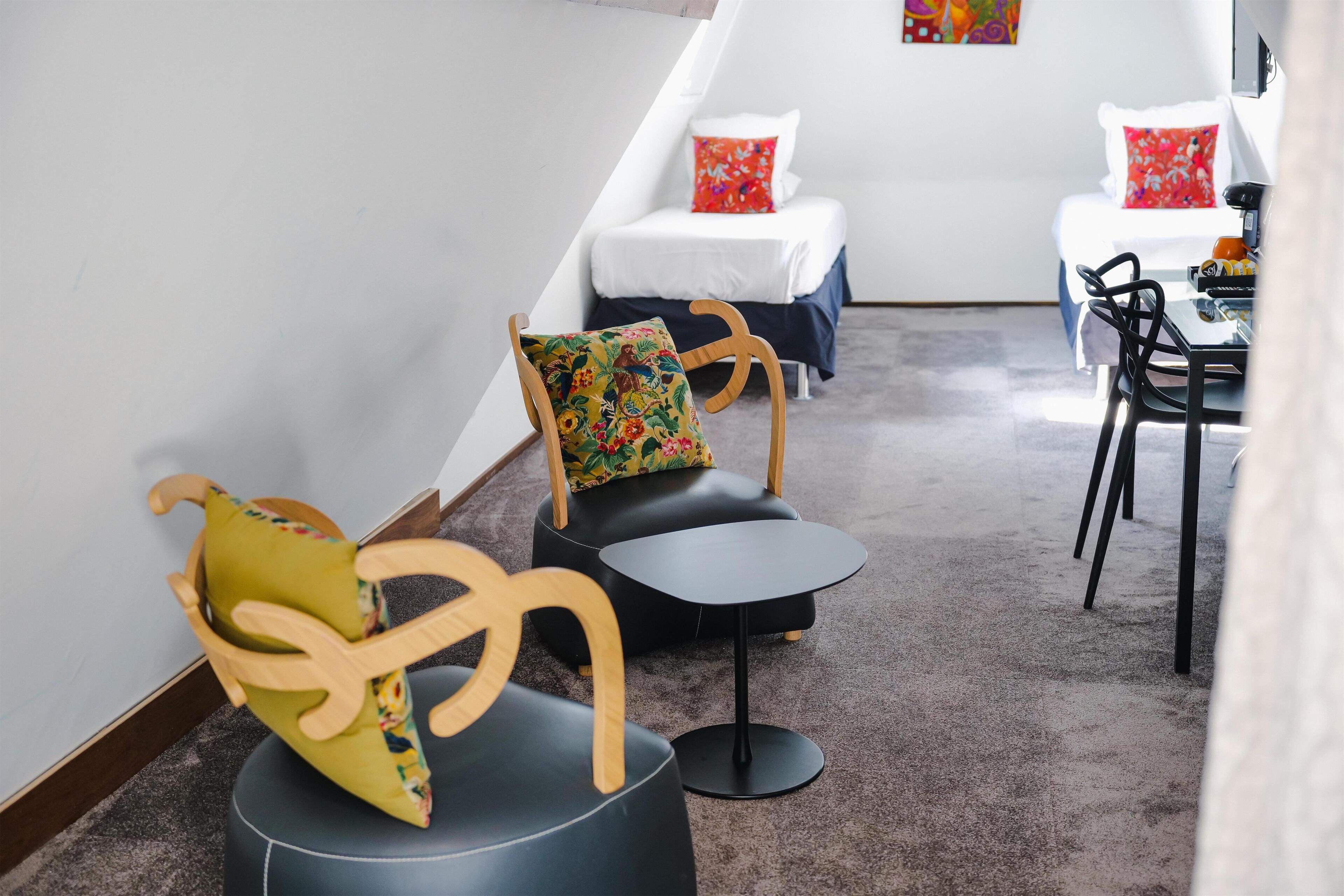 Et hotelværelse med en seng, to stole, et lille bord og et fjernsyn.