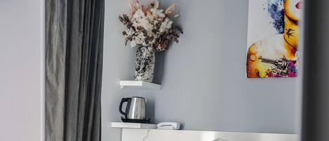 Habitación de hotel moderna con una cama bien hecha, un florero con flores secas, una cafetera y un cuadro en la pared.