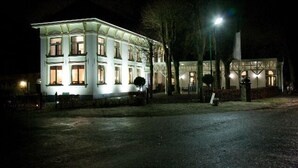 A large, illuminated building with multiple windows and a prominent entrance. - Hotel Restaurant het Rechthuis (Muiderberg)