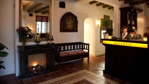 A lobby with a fireplace, a bench, a reception desk, and a large mirror. - Hotel Restaurant het Rechthuis (Muiderberg)