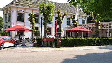 Enjoy outdoor seating under the shade of two umbrellas at this charming European-style building, home to a restaurant and surrounded by lush greenery.