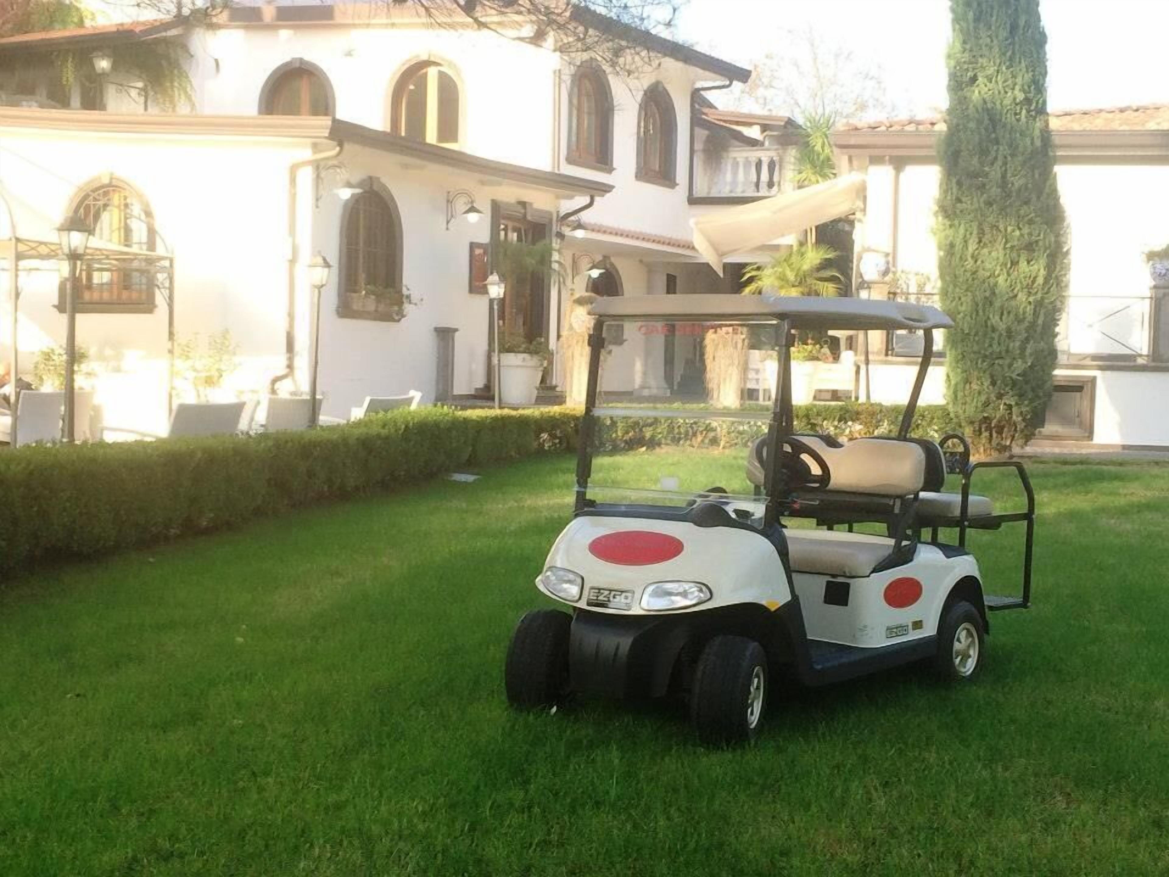 A golf cart parked on a well-maintained lawn in front of a white building with arched windows and a balcony.