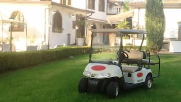 A golf cart parked on a well-maintained lawn in front of a white building with arched windows and a balcony.
